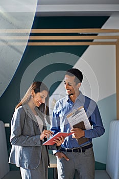 Two happy diverse workers talking standing in office. Vertical shot