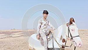 happy smiling Joyful man riding a white horse on a sandy terrain desert raising arms in excitement under a clear sky