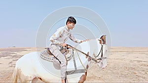 happy smiling Joyful man riding a white horse on a sandy terrain desert raising arms in excitement under a clear sky