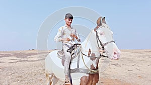 happy smiling Joyful man riding a white horse on a sandy terrain desert raising arms in excitement under a clear sky