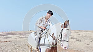 happy smiling Joyful man riding a white horse on a sandy terrain desert raising arms in excitement under a clear sky