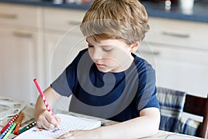 Happy smiling kid boy at home making homework writing letters with colorful pens