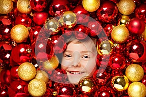 Happy Smiling Kid with Christmas Balls Toys. Child over Red and Golden Bauble Background. Shining Bright Xmas Tree Holiday
