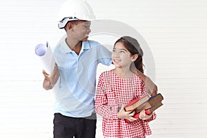 Happy smiling kid engineer African boy with helmet safety hat holding blueprint and cute Asian girl holding pile books standing