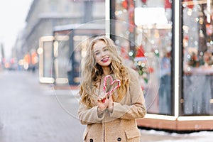 A happy smiling lady poses at a street holiday fair, holding lollipops in her hands. A funny girl makes a heart out of lollipops