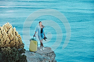 Happy smiling lady standing on sea view. Yellow luggage for journey. New ground and business travel concept, copy space