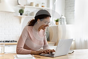 Happy smiling latin female writer in glasses typing on pc