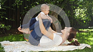 Happy smiling and laughing mother with baby son playing in garden while lying on grass. Parenting, family, children