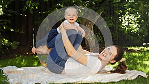 Happy smiling and laughing mother with baby son playing in garden while lying on grass. Parenting, family, children