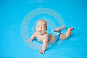 Happy, smiling little baby boy lying in blue swimming pool in water