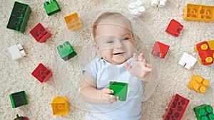 Happy smiling little baby boy lying on carpet covered with colorful toys, blocks and bricks. Concept of children