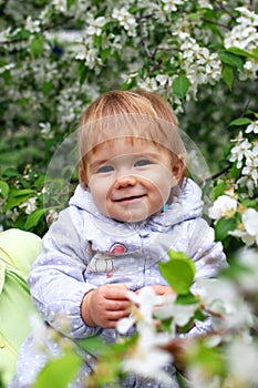 Happy smiling little baby girl in motherâ€™s hands on background of blooming garden with apple trees