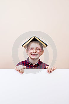 Happy smiling little boy with a book on his head, showing white