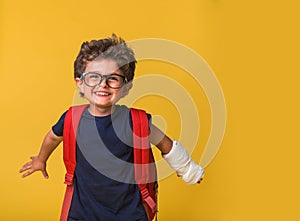 Happy smiling little boy in a cast. Kindergarten child with a broken arm isolated on yellow background. Funny kid after