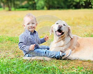 Happy smiling little boy child and Golden Retriever dog sitting on grass