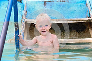 Happy smiling little boy coming into water in swimming pool