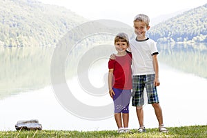 Happy smiling little boy and girl brother and sister standing hugging in sunny spring day near big lake in mountains