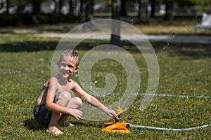 Happy smiling little boy play in water drops from irrigation hose