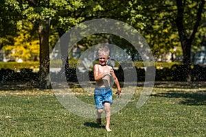 Happy smiling little boy play in water drops in the park, heat in the city