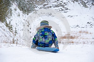 Happy smiling little boy slide down the ice slide, sits on an inflatable tubing. Cute little happy child having fun