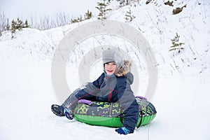 Happy smiling little boy slide down the ice slide, sits on an inflatable tubing. Cute little happy child having fun