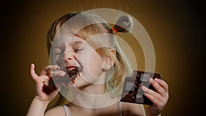 Happy smiling little child girl kid eating milk chocolate bar dessert isolated on dark background