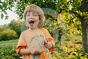 Happy smiling little child with green young pad peas in garden. Healthy eating, vegetables, legumes. Funny boy eating