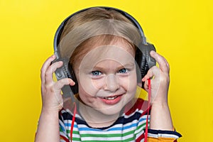 Happy smiling little child listening to music with headphones on yellow background