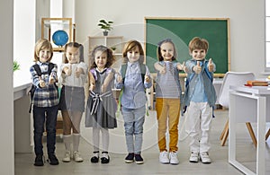 Happy smiling little children showing thumbs up standing in school classroom