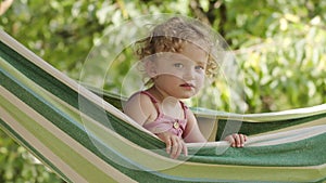 Happy smiling little girl with blue eyes and curly blonde hair enjoys playing hide and seek looking at camera. Child lying on the