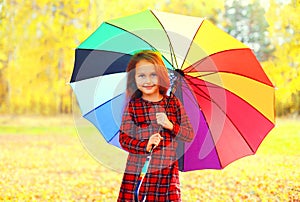 Happy smiling little girl child with colorful umbrella in sunny autumn