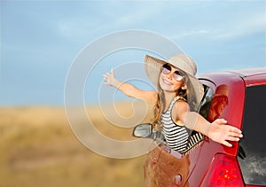 Happy smiling little girl child goes to summer travel trip in the red car