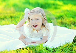 Happy smiling little girl child lying on grass in sunny summer