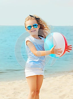 Happy smiling little girl child playing with inflatable water ball on beach near sea