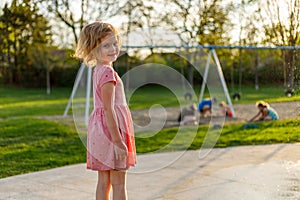 Happy smiling little girl and children playing at playground in park in summer