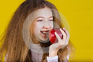 Happy, smiling little girl holding an red apple, eating it isolated on yellow background.Healthy food,Dental health.