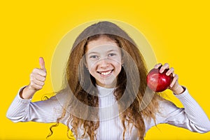 Happy, smiling little girl holding an red apple, and thumb up is