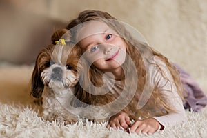 Happy smiling little girl hugging a dog Shih Tzu at home