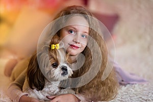 Happy smiling little girl hugging a dog Shih Tzu at home