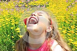 Happy smiling little girl with a red bow in her curly hair. Girl on a green meadow among yellow flowers