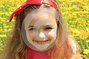 Happy smiling little girl with a red bow in her curly hair. Girl on a green meadow among yellow flowers