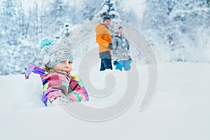 Happy smiling little girl sitting in deep snow when she walking with family in winter snowy forest