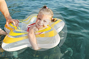 Happy smiling little girl swimming with swimring in the sea