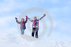 Happy smiling little girls wearing a warm clothes having fun against the blue sky on a snow in winter