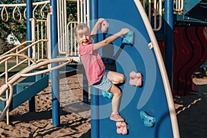 Happy smiling little preschool girl climbing rock wall at playground outside on summer day. Happy childhood lifestyle concept.