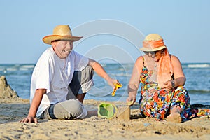 Happy smiling & looking at camera mature couple playing at seashore on sandy beach
