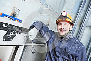 Smiling machinist with spanner adjusting lift in elevator shaft