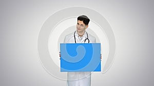 Happy smiling male doctor showing blank signboard and dancing on gradient background.