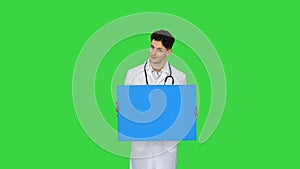 Happy smiling male doctor showing blank signboard and dancing on a green screen, chroma key.
