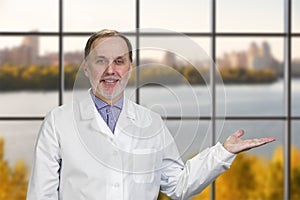 Happy smiling male senior doctor advertising a copy space.